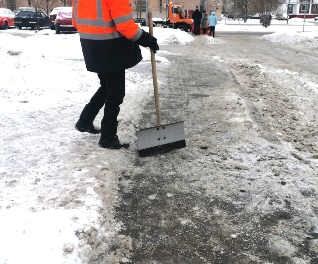 Faceless Janitor cleans the pavement from snow and ice with a shower in winter